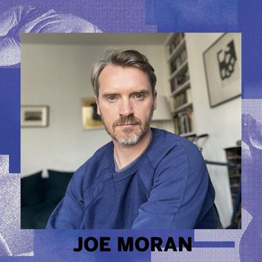 An image of Joe Moran on a blue background with her name below. Image description: Joe Moran, courtesy of the artist Portrait of a white man with short light brown hair and a trimmed beard, wearing a blue sweatshirt, seated indoors and looking directly at the camera, with bookshelves and artwork in the background.