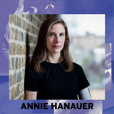 An image of Annie Hanauer on a blue background with her name below. Image description: Annie, a white woman in her late 30s with shoulder-length light brown and grey hair and blue-green eyes, standing next to a brick wall, looking straight into the camera with a relaxed neutral expression. She's wearing a black t-shirt and on her left upper arm a white sock that fits under her prosthetic. Light spills in from the right side of the frame and through a blurry window in the background.