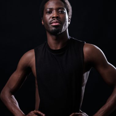 Isaac Ouro-Gnao standing in a black tank top with hands on his hips.