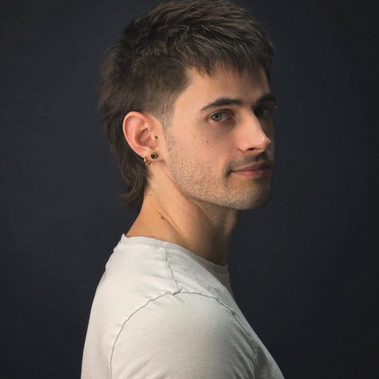 A man in a white t-shirt, he is facing the right but his head is turned towards the camera.
