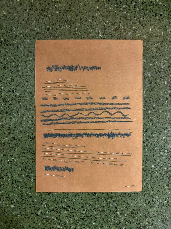 Brown cardstock sheet with rows of pen or marker strokes, including scribbles, dashed lines, straight lines, and wavy patterns, on a speckled surface.