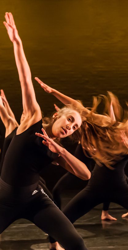 A group of secondary school students on The Place stage wearing black tops and trousers dancing