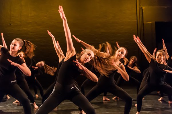 A group of secondary school students on The Place stage wearing black tops and trousers dancing