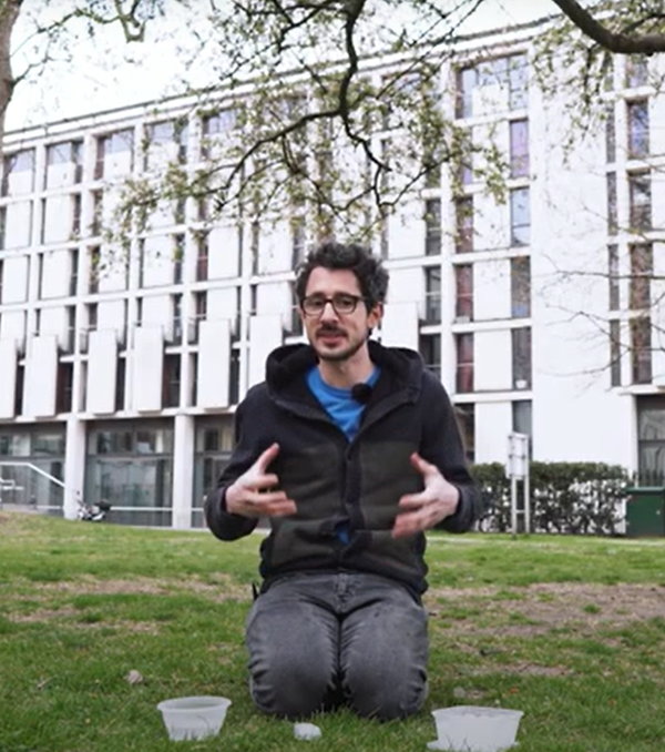 Person sitting on grass with 2 bowls of water. They are holding their hands out in front of them explaining something.