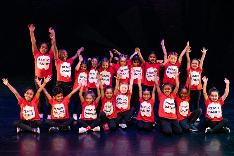 A group of children wearing red T-shirts saying 'RemixDance' raising their arms overhead