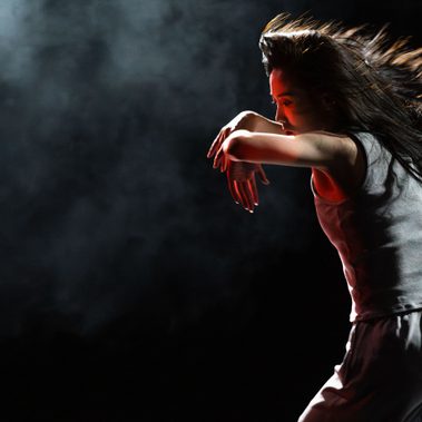 A young person wearing white dances on a black background
