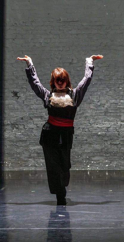 A single dancer stands half in shadow with their arms raised