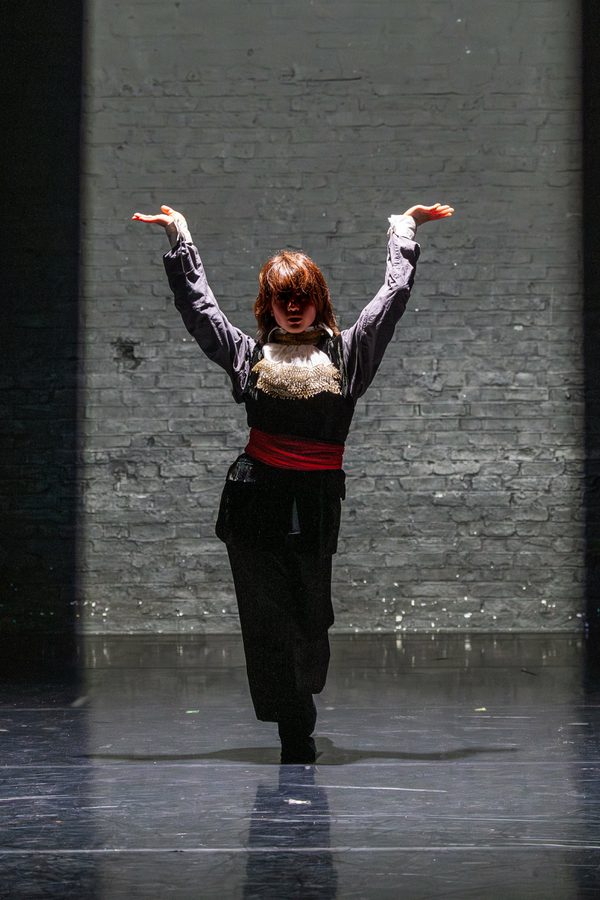 A single dancer stands half in shadow with their arms raised