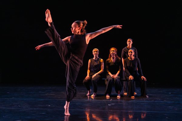 4 women are seated, watching a 4th dance a high kick