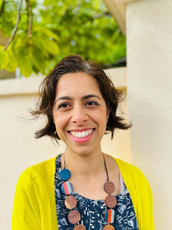 Image of Shaparak Rahimi. Shaparak has dark hair and is wearing a yellow cardigan and a blue top. She is smiling.