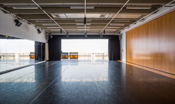 Image of an empty studio with wooden panels on the right, a window at the back and mirrors on the left