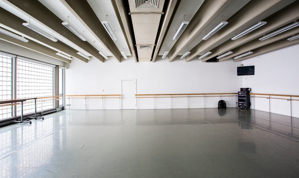 Image of an empty studio with ballet bar on the far wall, windows on the left