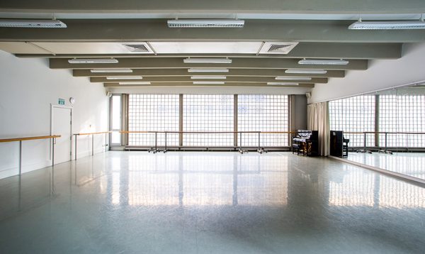image of an empty studio with mirrors on the right hand side, windows on the far walls with ballet barres across the windows and along the left wall