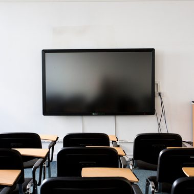 A lecture room is set up with individual chairs with desks facing a screen.