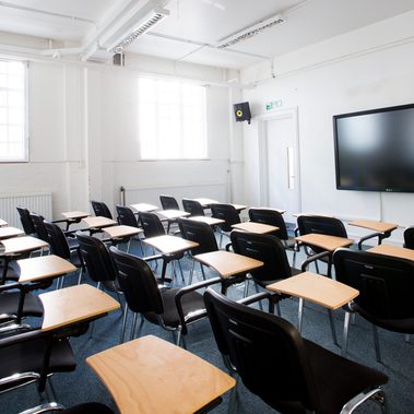 A lecture room is set up with individual chairs with desks facing a screen.