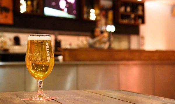 A photo of the theatre bar at The Place. We see a wooden table with a pint of meantime beer on it. The bar is in the background.