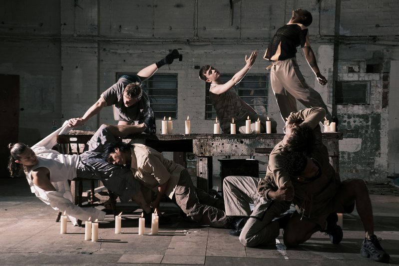 Six individuals positioned around a table surrounded by candles