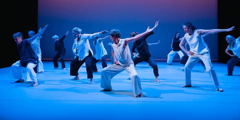 A company over of Over 60s dancers on stage in front of a sunset background.