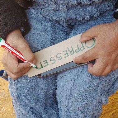 Looking from above, a person sitting in a wheelchair writes a sign saying oppression.