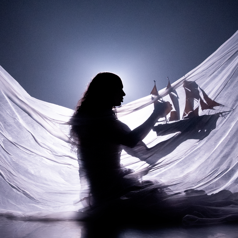 Silhouette of Little M, a person with long hair, wearing a draped flowing translucent fabric, holding a model ship with red sails. Backlit to create a dreamy, underwater-like glow, the image evokes a sense of a dreamlike world.