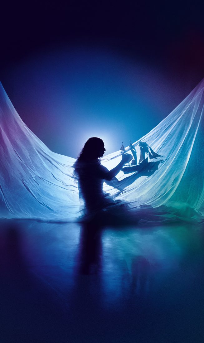 Silhouette of Little M, a Silhouette of Little M, a person with long hair, wearing a draped flowing translucent fabric, holding a model ship with red sails. Backlit to create a dreamy, underwater-like glow, the image evokes a sense of a dreamlike world. with long hair, wearing a draped flowing translucent fabric, holding a model ship with red sails. Backlit to create a dreamy, underwater-like glow, the image evokes a sense of a dreamlike world.
