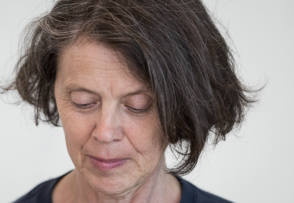 A close up of a woman's face with dark medium length hair looks downs