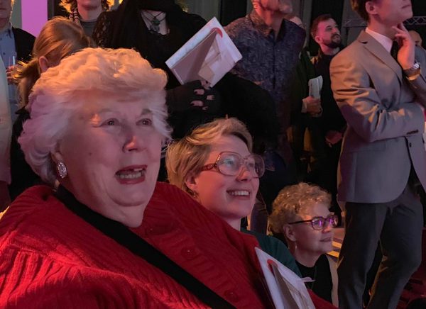 A group of people appear to be watching something in the distance, there are two woman are smiling, one is older and the other is younger