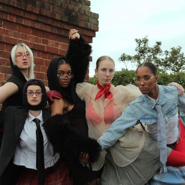 5 dancers pose with limbs intertwined with one another. All wear a mixture of textured and coloured clothing.