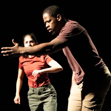 One of the performers stretches his hand in front of him with palm open, while the other is looking at the hand and in motion to grab it.