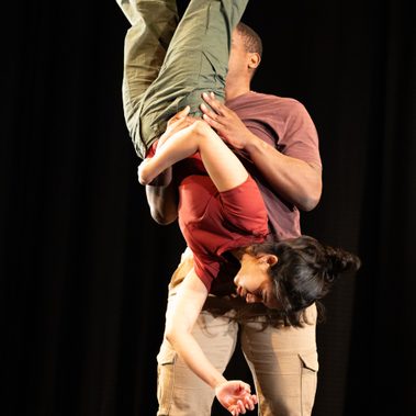 A performer is being lifted upside down by the other, and she hangs in mid-air.