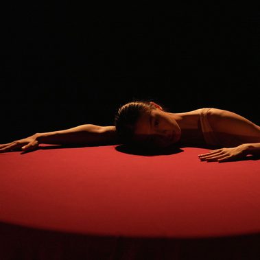 In the dim light, a woman sprawled on a table covered with red tablecloth.
