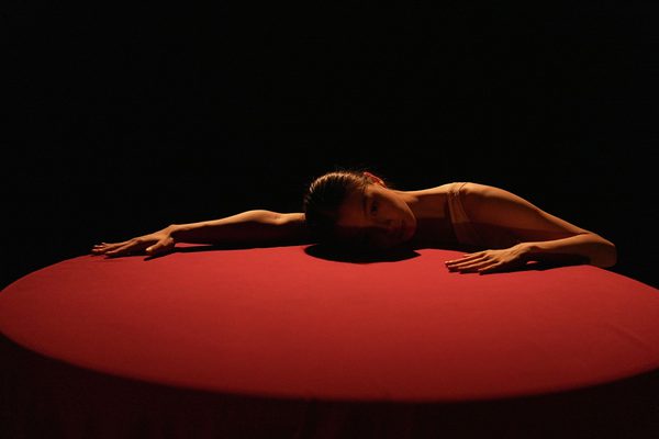 In the dim light, a woman sprawled on a table covered with red tablecloth.