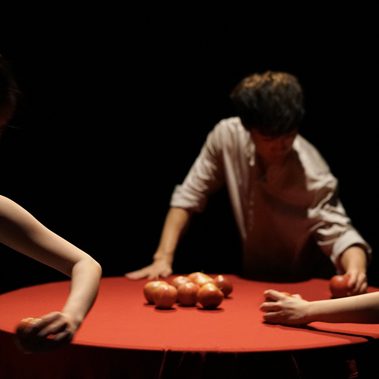 Three dancers gathered around a round table holding apples in their hands.