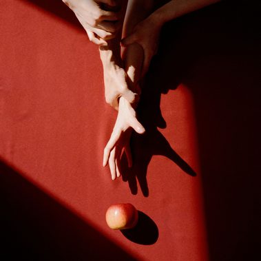 One hand tried to grasp the apple, and the other three hands interlaced over it.