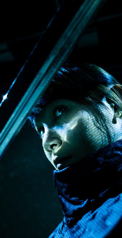 Close-up of a woman gazing from beneath a sword blade that partially covers her face.
