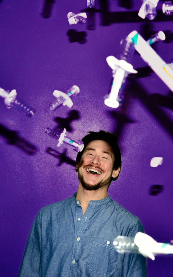Man shown from the shoulders up laughing against a purple background, surrounded by flying syringes.