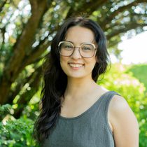 Sophia's headshot against a leafy green backdrop on a sunny day