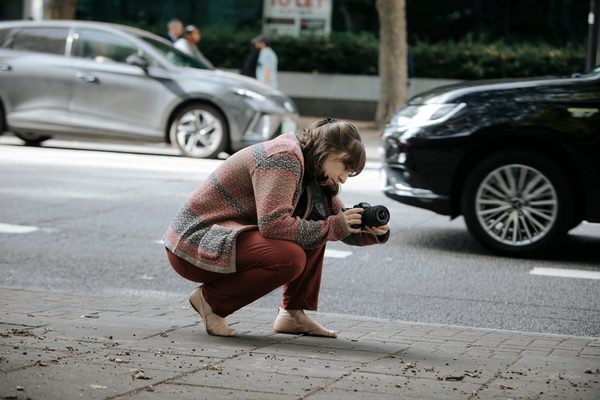 Student with a camera, kneeled down on the street to capture a shot