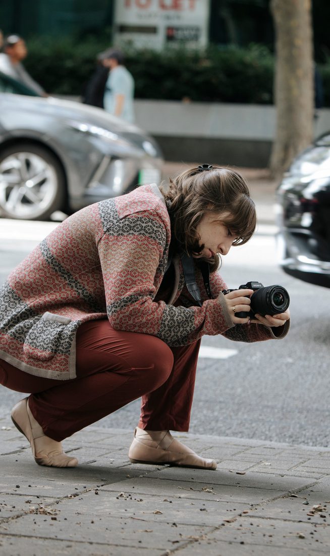 Student with a camera, kneeled down on the street to capture a shot