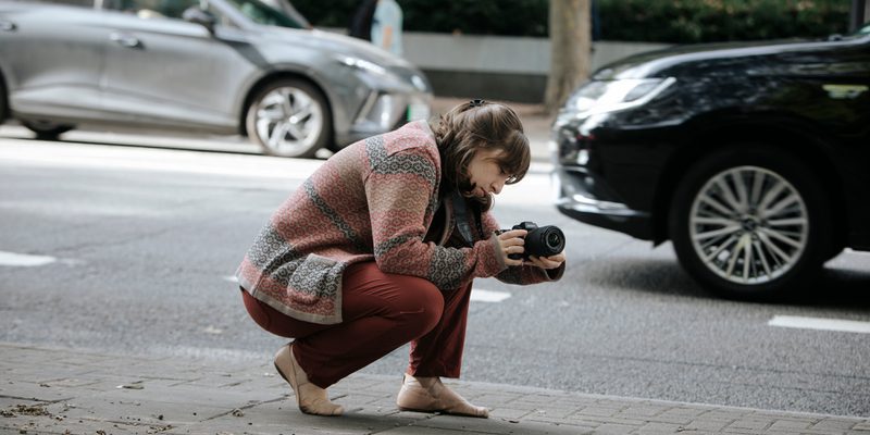 Student with a camera, kneeled down on the street to capture a shot