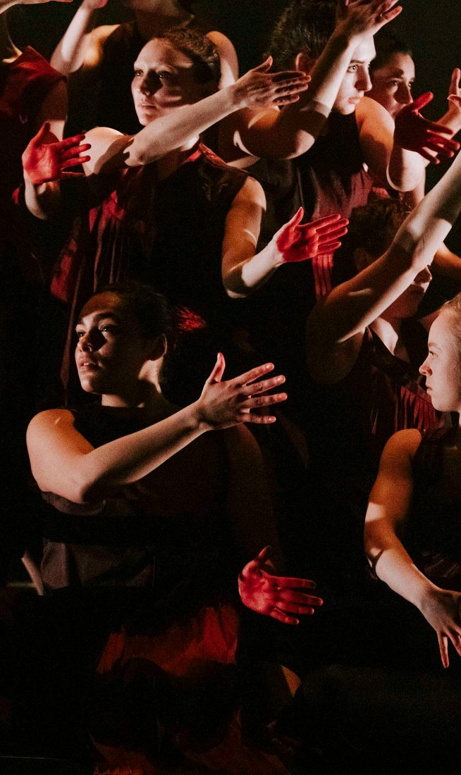 A kaleidoscopic image of dancers stood at different levels, dressed in black and holding up a hand painted red.
