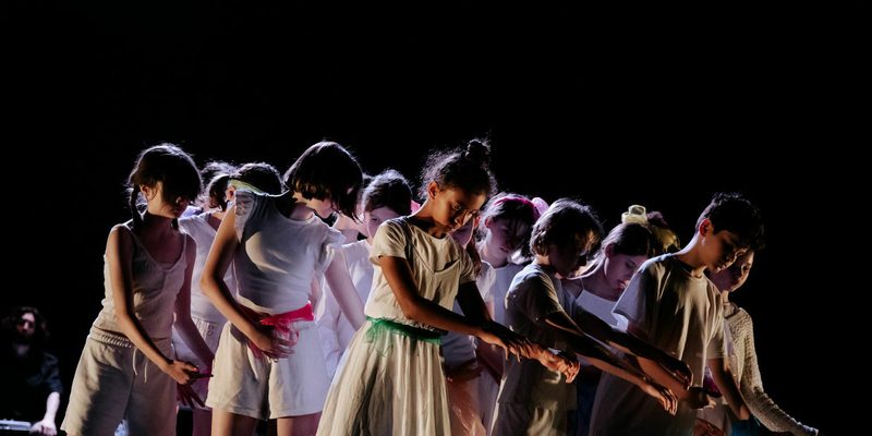 A group of young dancers wearing white and moving in sync in the stage.