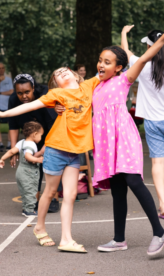 Children in a dance workshop outside. Two girls are dancing together and smiling.