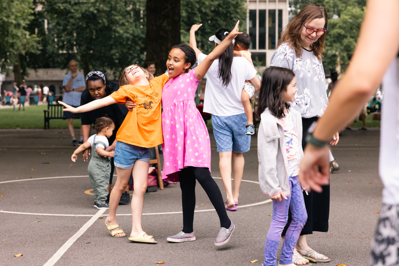 Children in a dance workshop outside. Two girls are dancing together and smiling.