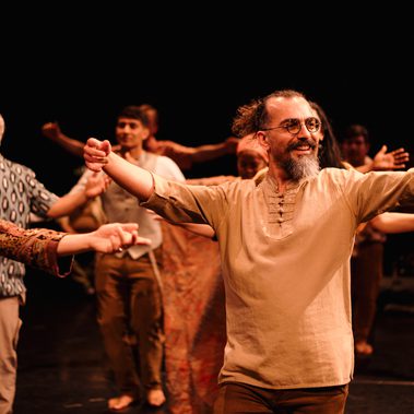 A group of performers are on stage with their arms out wide. All the performers are smiling.