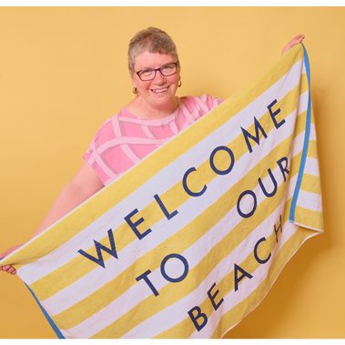A solo performer holds up a towel that says Welcome to Our Beach
