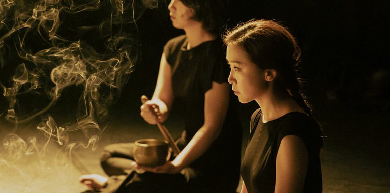 Two musicians dressed in black playing instruments, with incense wafting in the air.