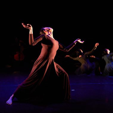 The image shows three female dancers with one at the front, but her face is stretched upwards and two at the back kneeling facing away also looking upwards – all three with their hands outstretched and their faces turned upwards coming out of a harrowing experience.