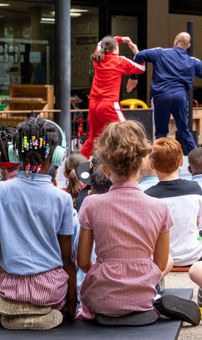 Two school girls watching two adults dance in a playground setting.